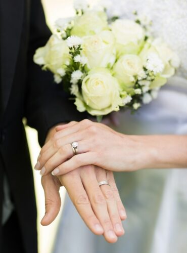 Closeup of bride and groom showing wedding rings touching hands